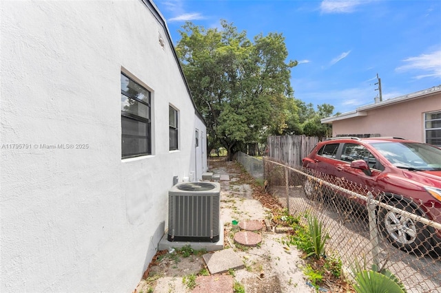 view of side of property with stucco siding, fence, and cooling unit
