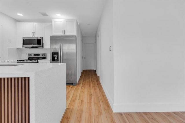 kitchen with baseboards, light wood finished floors, stainless steel appliances, recessed lighting, and white cabinetry