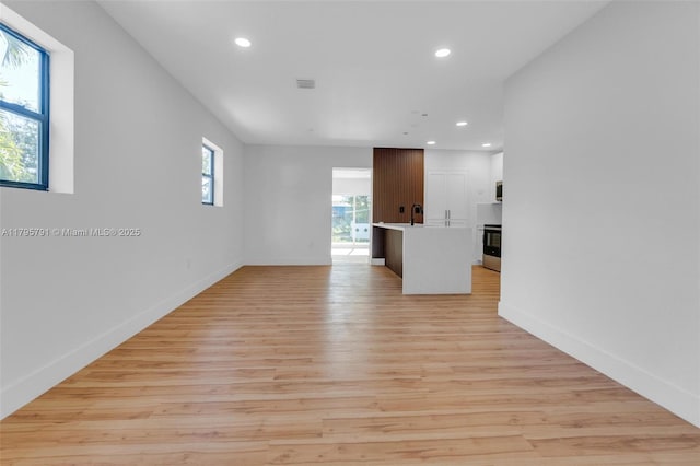 unfurnished living room with visible vents, a sink, baseboards, light wood-style floors, and recessed lighting