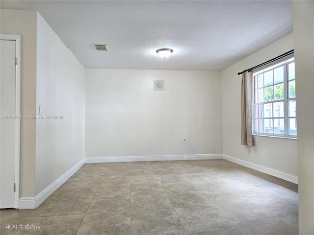 empty room with visible vents, a textured ceiling, and baseboards