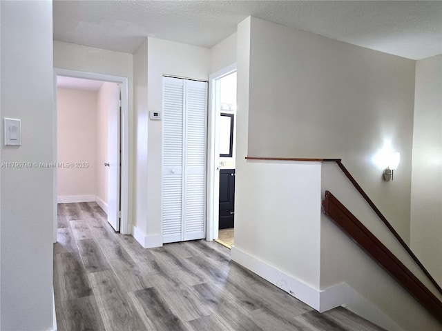 corridor featuring baseboards, wood finished floors, and an upstairs landing
