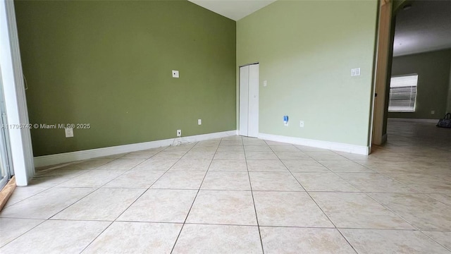 empty room featuring high vaulted ceiling, baseboards, and light tile patterned flooring