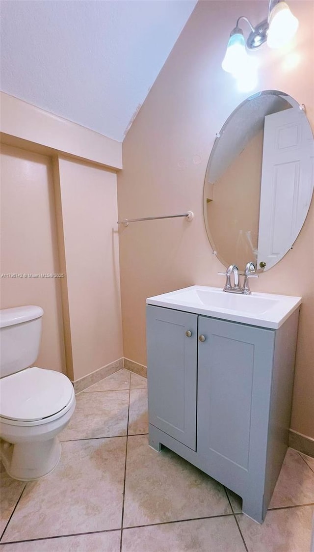 half bathroom with vanity, tile patterned flooring, vaulted ceiling, and toilet