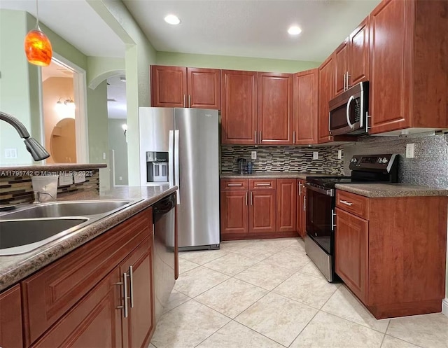 kitchen with light tile patterned flooring, appliances with stainless steel finishes, a sink, arched walkways, and decorative backsplash