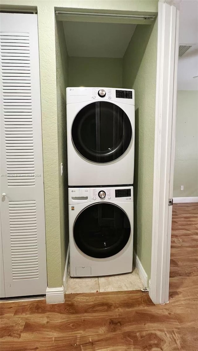 laundry room featuring stacked washer and dryer, baseboards, wood finished floors, and a heating unit