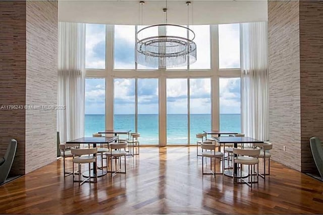 dining area featuring wood finished floors, a wall of windows, a high ceiling, a water view, and a chandelier