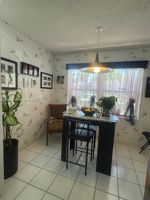 dining area featuring light tile patterned floors, wallpapered walls, and a textured ceiling