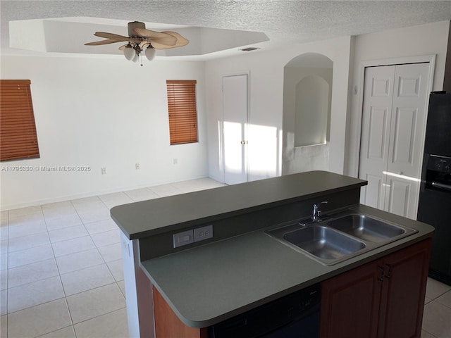 kitchen featuring dark countertops, a sink, light tile patterned floors, black appliances, and an island with sink