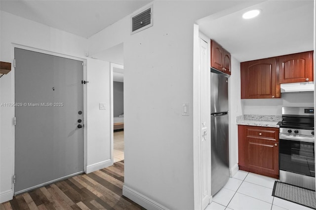 kitchen with light wood finished floors, stainless steel appliances, baseboards, under cabinet range hood, and visible vents
