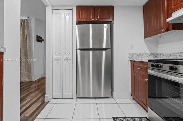 kitchen with baseboards, appliances with stainless steel finishes, under cabinet range hood, and light tile patterned floors