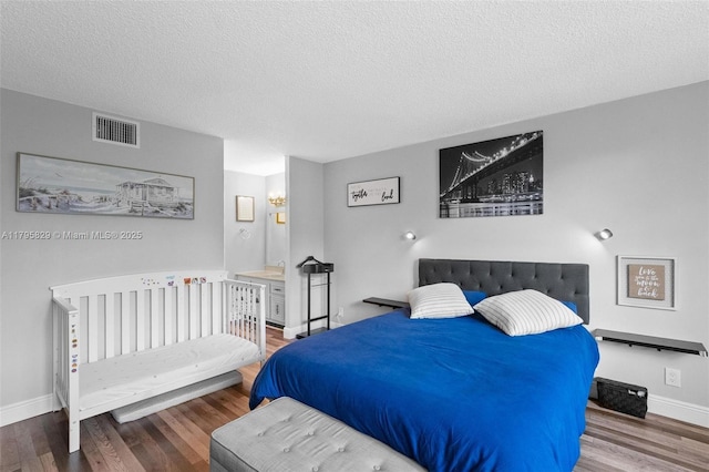 bedroom with visible vents, a textured ceiling, baseboards, and wood finished floors