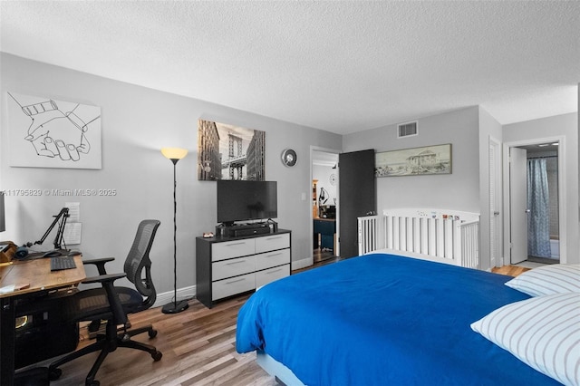 bedroom with baseboards, a textured ceiling, visible vents, and wood finished floors