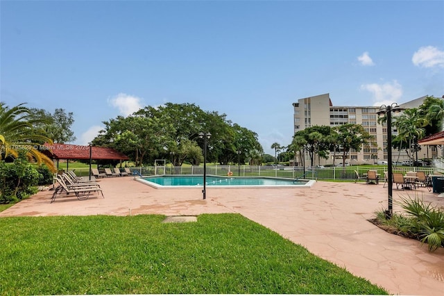 community pool with a patio area, fence, and a yard