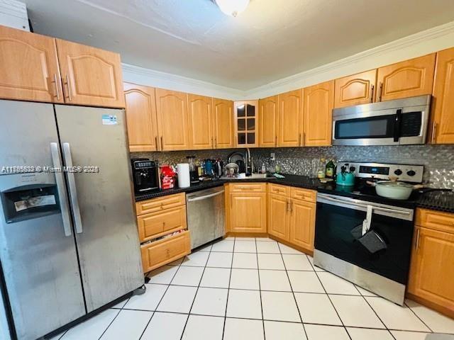 2780 NE 183rd St Unit 810, Aventura, FL 33160 - kitchen with stainless steel appliances, tasteful backsplash, dark countertops, glass insert cabinets, and light tile patterned floors