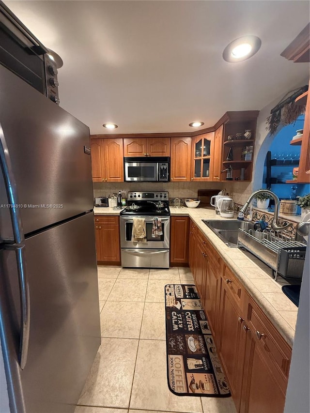 401 Ocean Dr Unit 324, Miami Beach, FL 33139 - kitchen with stainless steel appliances, brown cabinets, light countertops, light tile patterned floors, and backsplash