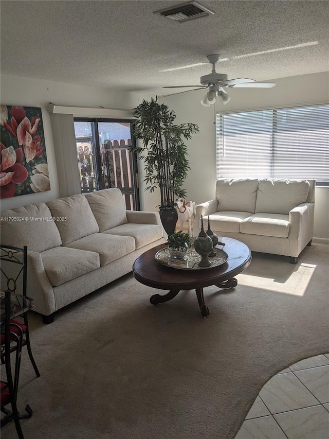 carpeted living area featuring a textured ceiling, ceiling fan, and visible vents