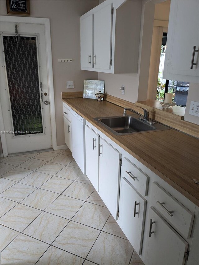 kitchen with a sink, butcher block counters, dishwasher, light tile patterned floors, and white cabinets