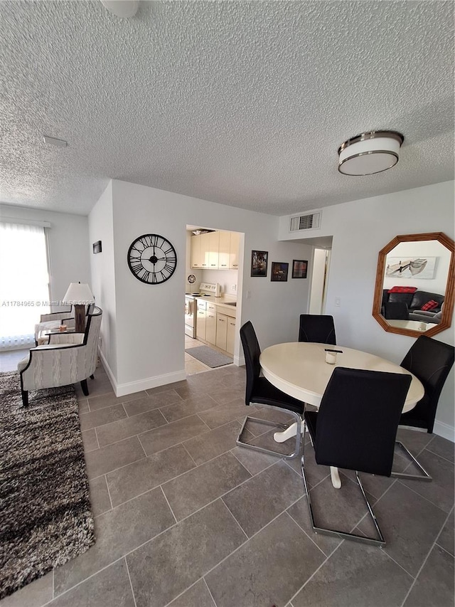 dining space featuring dark tile patterned floors, a textured ceiling, visible vents, and baseboards