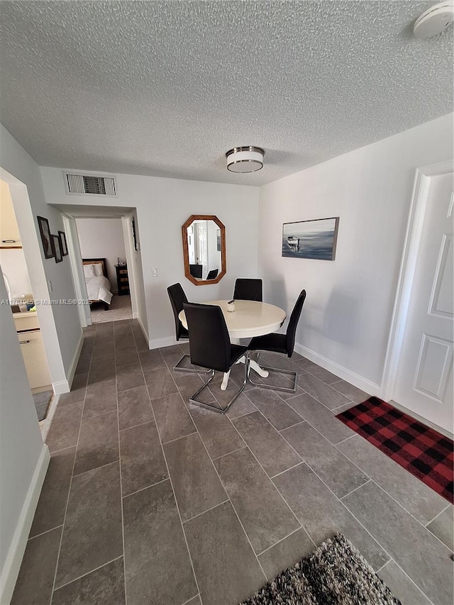 dining area with dark tile patterned flooring, baseboards, a textured ceiling, and visible vents