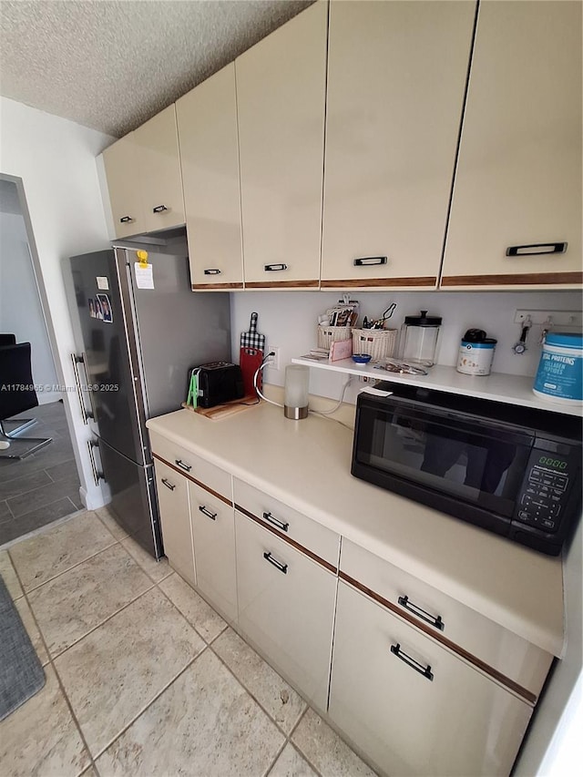 kitchen with light countertops, white cabinets, black microwave, and freestanding refrigerator