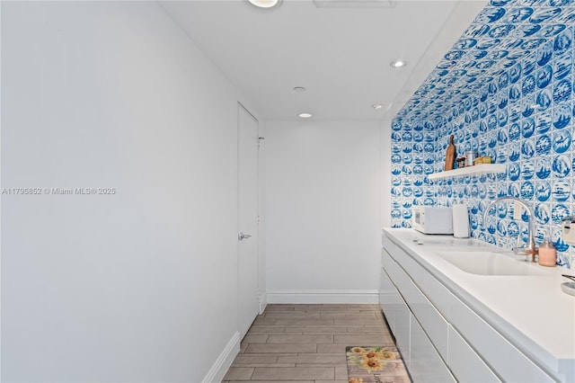 bathroom featuring baseboards, recessed lighting, wood finished floors, and vanity