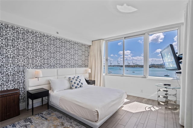 bedroom featuring baseboards, wallpapered walls, and wood finished floors