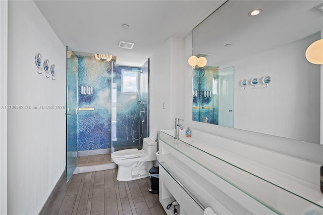 bathroom featuring vanity, toilet, wood finished floors, visible vents, and a stall shower