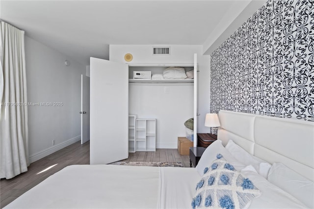 bedroom featuring baseboards, a closet, wood finished floors, and visible vents
