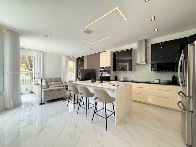 kitchen featuring freestanding refrigerator, wall chimney exhaust hood, modern cabinets, and a breakfast bar