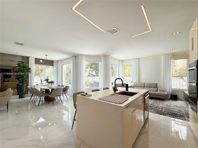 kitchen featuring visible vents, marble finish floor, open floor plan, a sink, and a wealth of natural light