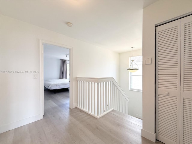 hallway featuring baseboards, wood finished floors, and an upstairs landing