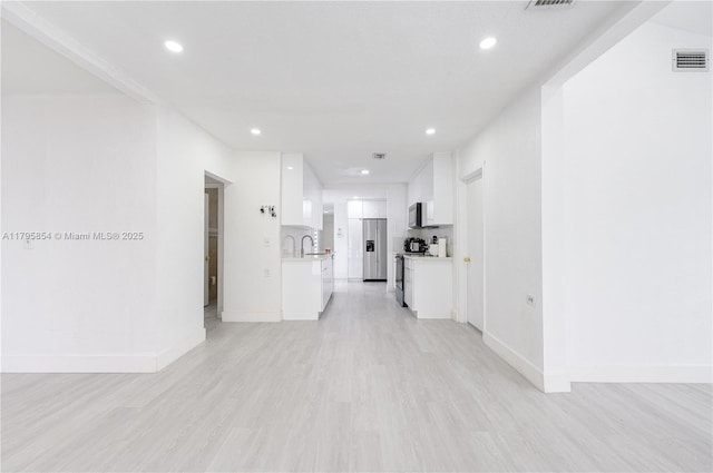 hallway featuring visible vents, baseboards, recessed lighting, light wood-type flooring, and a sink