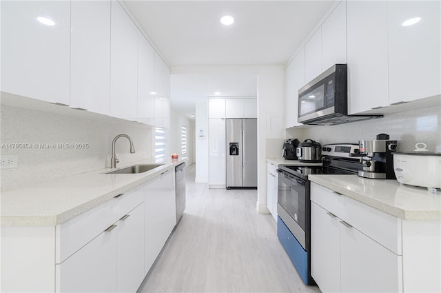 kitchen featuring appliances with stainless steel finishes, modern cabinets, light wood-type flooring, a sink, and white cabinets
