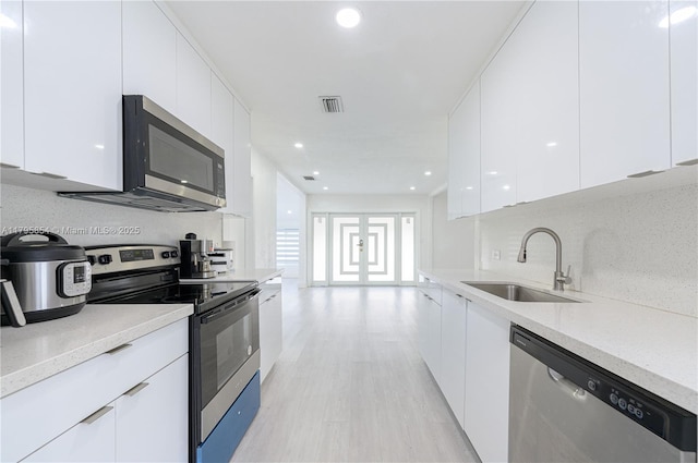 kitchen with modern cabinets, white cabinets, a sink, light wood-style flooring, and stainless steel appliances