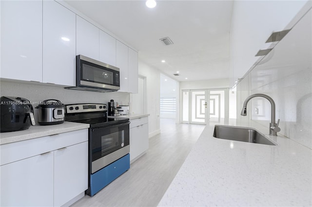 kitchen featuring light stone countertops, appliances with stainless steel finishes, a sink, white cabinetry, and visible vents
