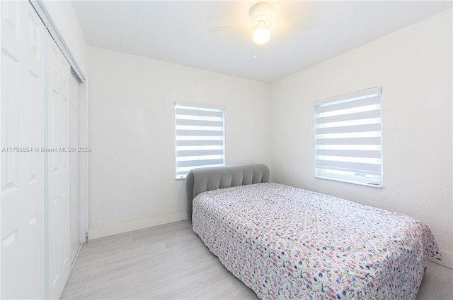 bedroom featuring baseboards, ceiling fan, light wood-style flooring, and a closet