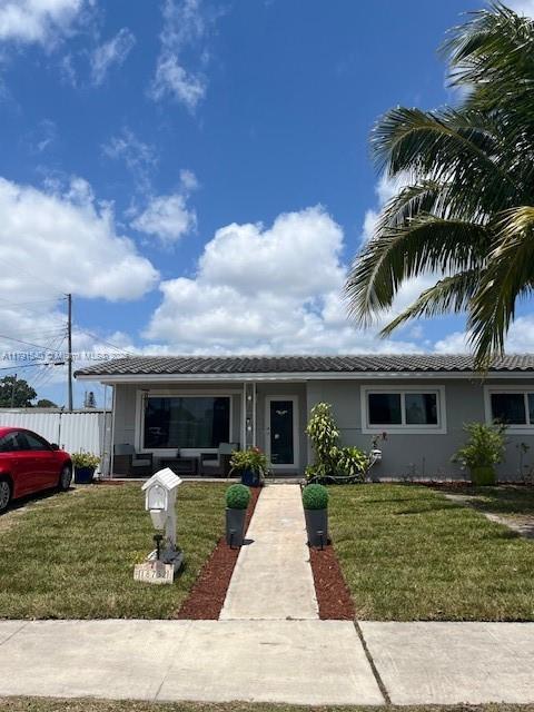 view of front facade featuring covered porch, a tiled roof, stucco siding, and a front lawn