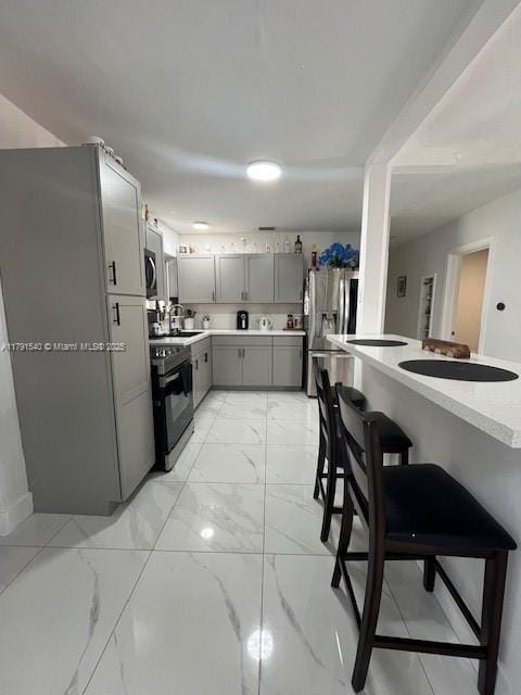 kitchen featuring marble finish floor, a breakfast bar area, light countertops, appliances with stainless steel finishes, and gray cabinetry
