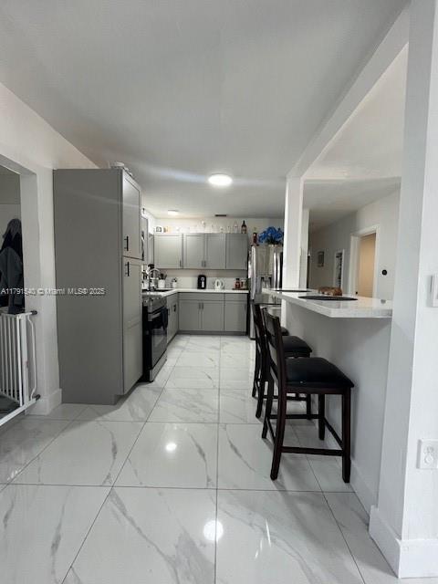 kitchen featuring marble finish floor, stainless steel refrigerator with ice dispenser, light countertops, gray cabinets, and electric stove