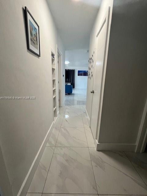 corridor featuring baseboards, built in features, and marble finish floor