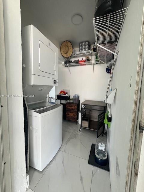 laundry area featuring stacked washer and dryer and marble finish floor