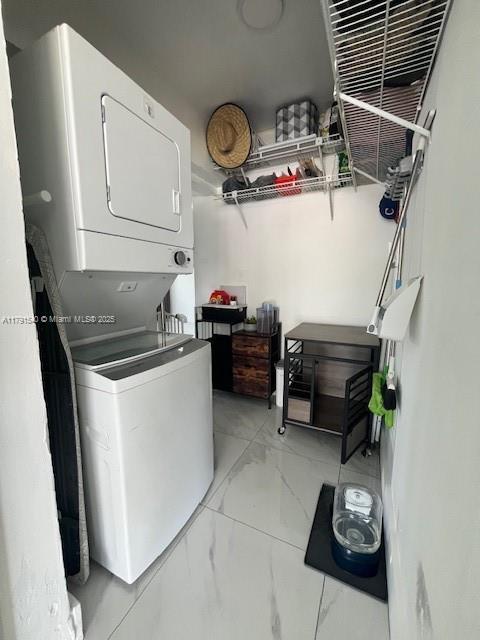 washroom with stacked washer and dryer and marble finish floor
