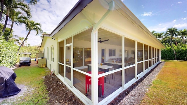view of side of home featuring a sunroom, a ceiling fan, and a yard