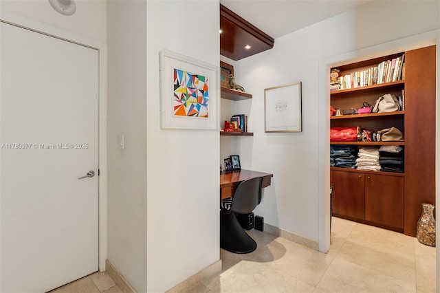hallway with a desk, light tile patterned flooring, and baseboards