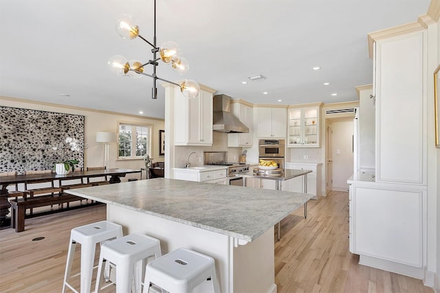 kitchen featuring a center island, decorative backsplash, light wood-style flooring, and wall chimney exhaust hood