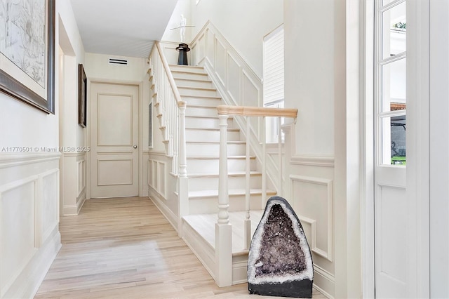stairs with a wainscoted wall, wood finished floors, and a decorative wall