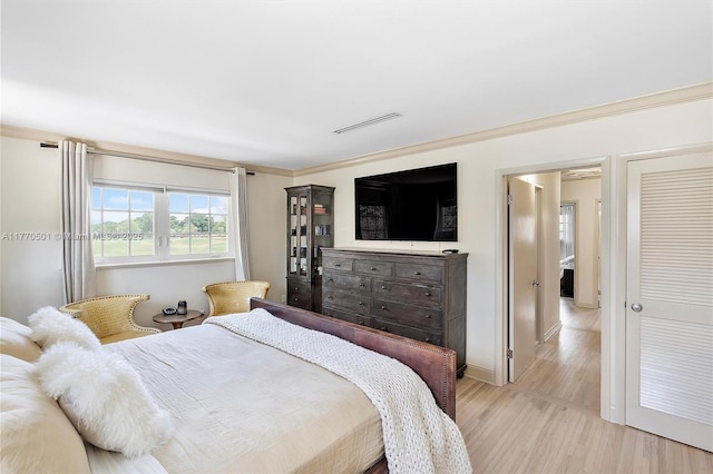 bedroom with baseboards, ornamental molding, light wood finished floors, and visible vents