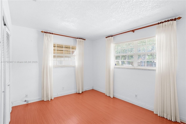 spare room with baseboards, a textured ceiling, and wood finished floors