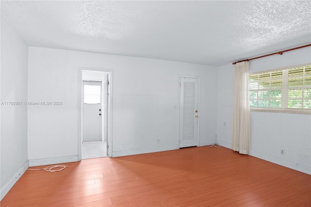 empty room featuring a textured ceiling, baseboards, and wood finished floors