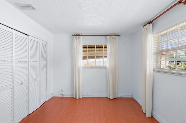 unfurnished bedroom featuring visible vents, a closet, light wood-style floors, baseboards, and a textured ceiling